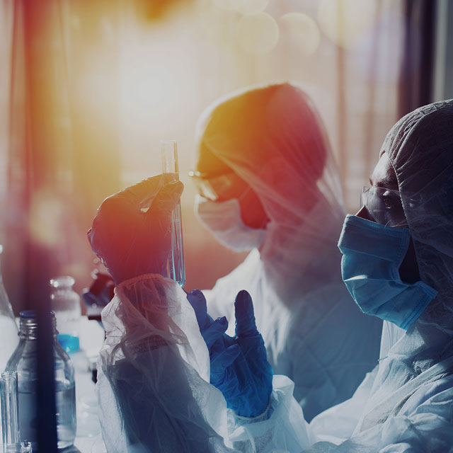 EIne Forschende mit Schutzanzug und Maske in einem Labor betrachtet ein Reagenzglas